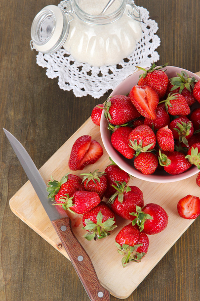 Strawberries in bowl on board cutting on wooden table - Foto, imagen