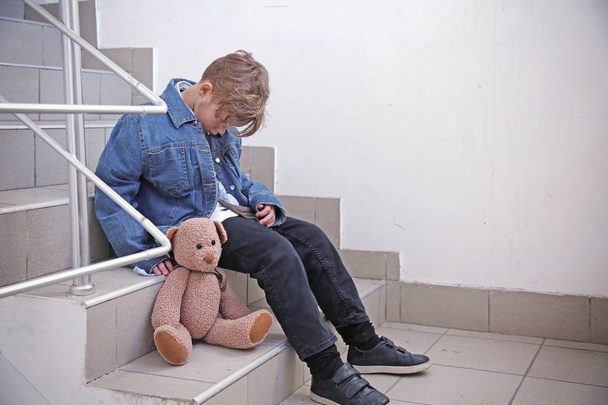 Merdivenlerde oyuncak ayı oturan evsiz küçük çocuk - Fotoğraf, Görsel
