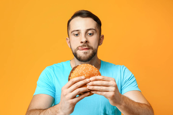 Man with burger on color background - Photo, Image