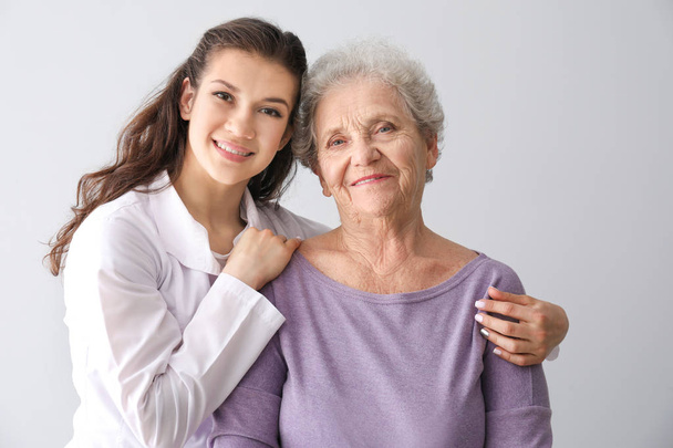 Médico joven con mujer mayor sobre fondo gris
 - Foto, Imagen