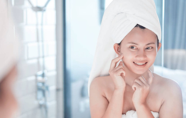 Close-up vrouw kijkt haar gezicht in de spiegel met glimlachen na bad, gezondheidszorg en schoonheid - Foto, afbeelding