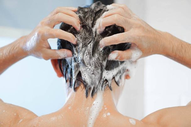 Nahaufnahme junger Mann beim Haarewaschen mit Shampoo im Badezimmer, Vintage-Ton, selektiver Fokus - Foto, Bild