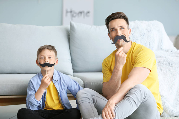 Portret van grappige vader en zoon met nep snor thuis - Foto, afbeelding