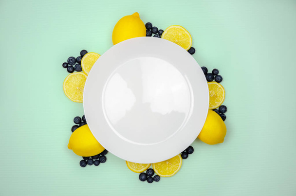 Arándanos frescos y limón en la vista superior con plato blanco
. - Foto, Imagen