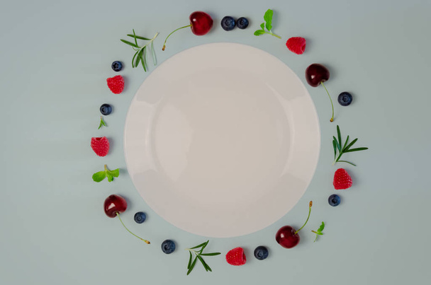 Fresh cherry, blueberry, raspberry, mint and rosemary leaf on top view with white plate. - Foto, immagini