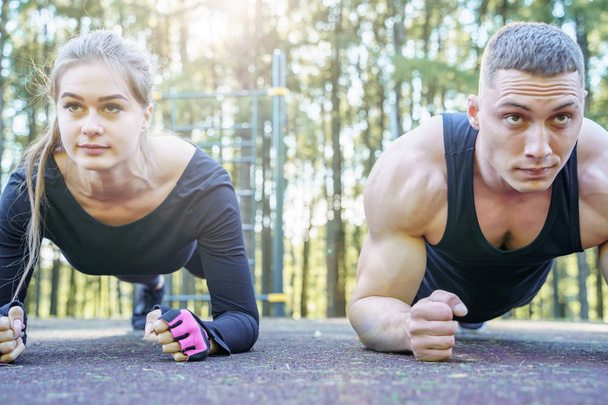 Portrait of young sporty couple doing the plank exercise outdoors. - Фото, изображение