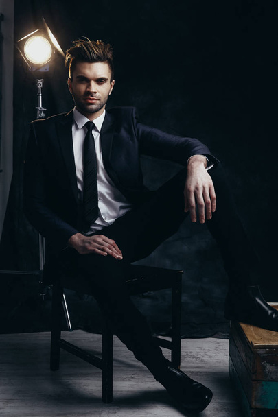 Portré csinos férfi ül egy stúdióban, fekete anyag háttér és a mozi fény. - Fotó, kép