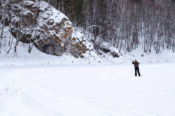 лыжник в зимнем лесу на лыжах вдоль скалы
 - Фото, изображение