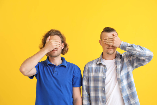 Nuoret miehet peittävät silmänsä värillisellä taustalla
 - Valokuva, kuva