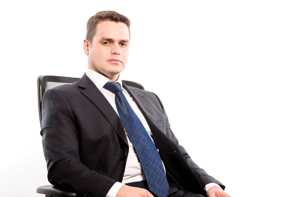 A serious man in a suit sits in a chair on a white background in - Foto, Bild