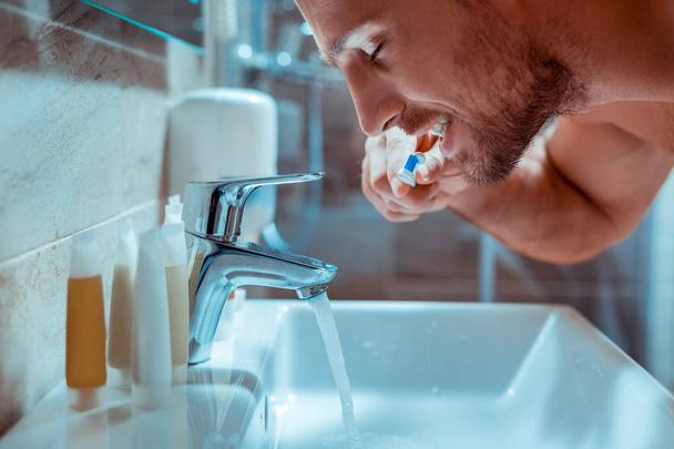 Accurate guy brushing his teeth during morning routine - Foto, afbeelding