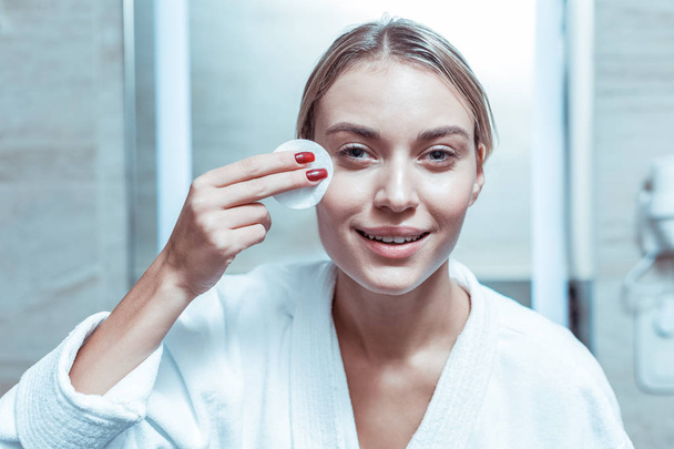 Good-looking woman with soft smile cleaning face with soaked cotton pad - Photo, Image