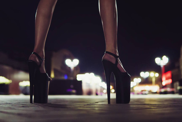 Hermosas piernas femeninas sexy elegante de cerca en la calle de la noche de la ciudad en el fondo de linternas brillantes. Zapatos de tacón alto para actuar en el escenario para Striptease
. - Foto, Imagen