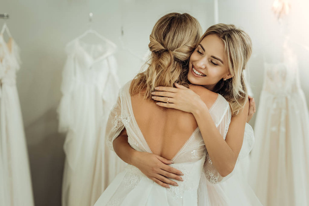 Two brides hugging each other in a wedding shop. - Φωτογραφία, εικόνα