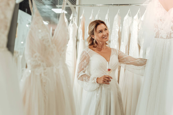 Beautiful bride touching dresses that hanging in the shop. - Фото, изображение