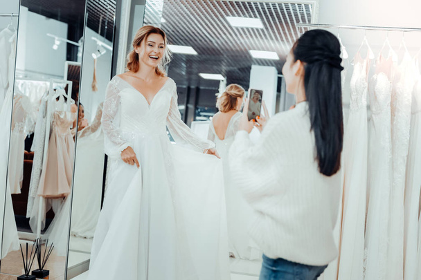 Beautiful bride and her bridesmaid taking pictures of a dress. - Fotó, kép