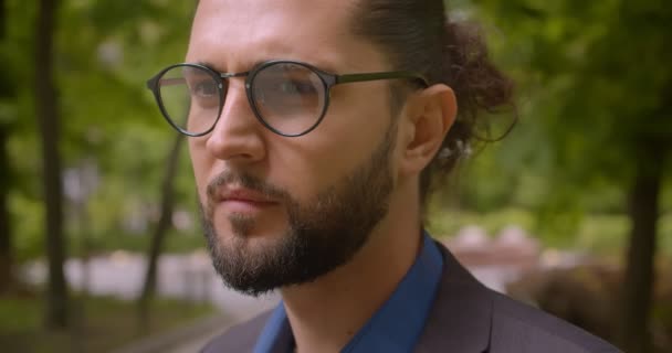 Close-up shot of handsome hipster guy in formal suit with ponytail smiling and flirting into camera in park. - Séquence, vidéo