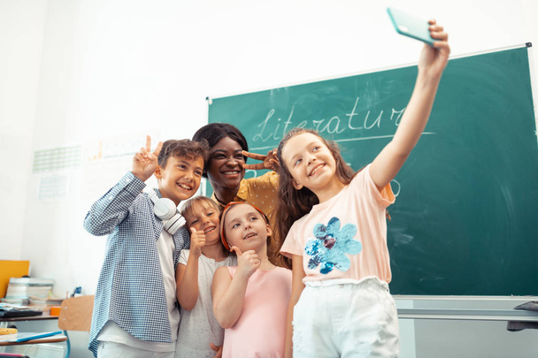 Δάσκαλος και παιδιά αισθάνονται ευτυχισμένοι ενώ φτιάχνουν selfie μαζί - Φωτογραφία, εικόνα