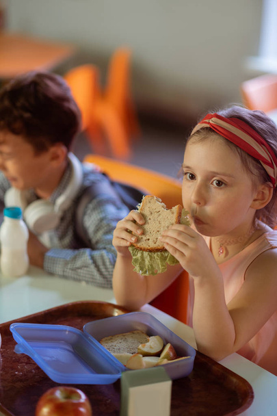 Beautiful cute schoolgirl eating delicious sandwich in canteen - Foto, Imagem