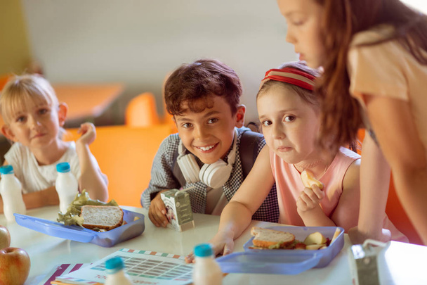 Boy smiling while sitting near girls having lunch together - Zdjęcie, obraz