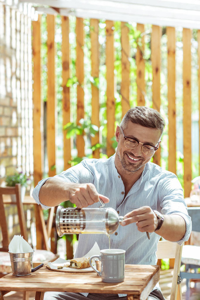 Smiling man drinking tea in a summer cafe. - Zdjęcie, obraz