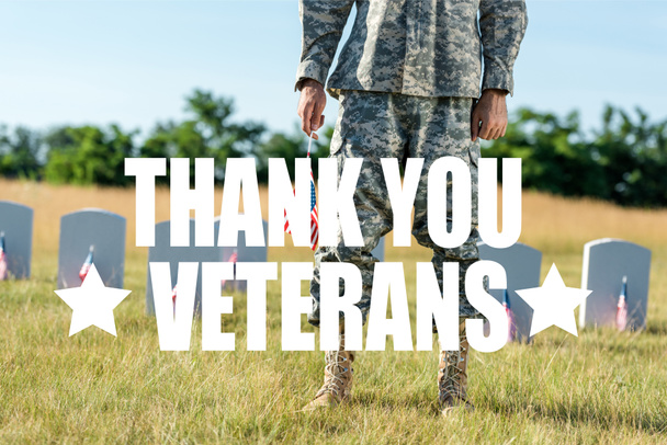 vista recortada de soldado en uniforme de camuflaje sosteniendo bandera americana y de pie en el cementerio con ilustración de los veteranos de gracias
 - Foto, Imagen