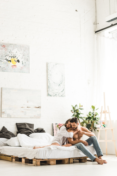 couple of people hugging while sitting in bedroom on bed  - Photo, Image