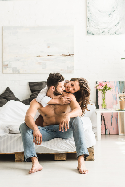 pareja joven sentada en la cama, abrazándose y mirándose
 - Foto, imagen