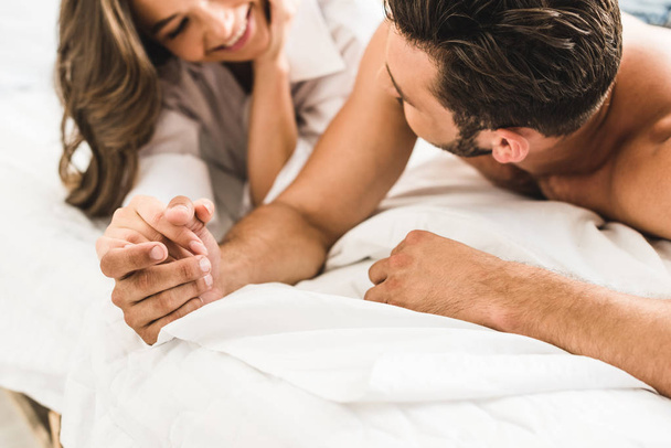 selektywnej koncentracji młodej pary leżącej w łóżku, trzymając ręce i patrząc na siebie - Zdjęcie, obraz