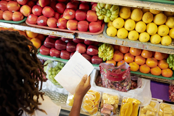 Donna con lista della spesa guardando scaffali con frutta e bacche al negozio di alimentari
 - Foto, immagini