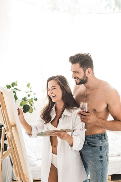 young couple laughing while girl drawing and boy holding glass with wine - Foto, Imagen