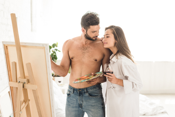 sexy Mann zeichnet, während Mädchen neben Freund hält und Glas mit Wein hält - Foto, Bild