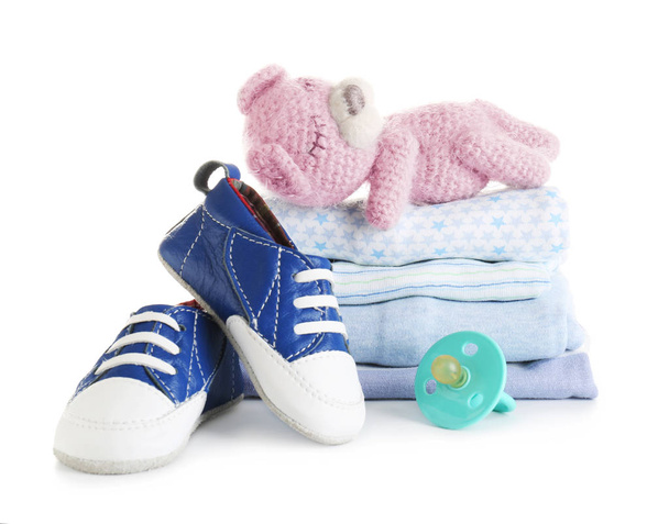 Stapel Babykleidung, Spielzeugbär und Schnuller auf weißem Hintergrund - Foto, Bild