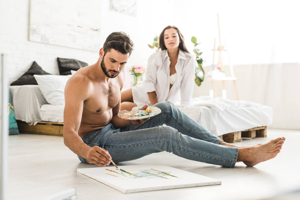 selective focus of couple sitting in bedroom while man drawing and girl looking at guy - Photo, Image