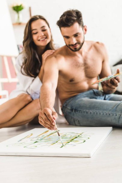 селективное внимание мужчины без рубашки рисует в то время как девушка сидит позади парня
 - Фото, изображение