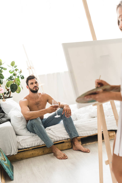 selective focus of man sitting in bed with wine and girl drawing with brush - Photo, Image