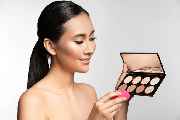 Asian woman with cosmetics for contouring makeup on light background - Fotó, kép