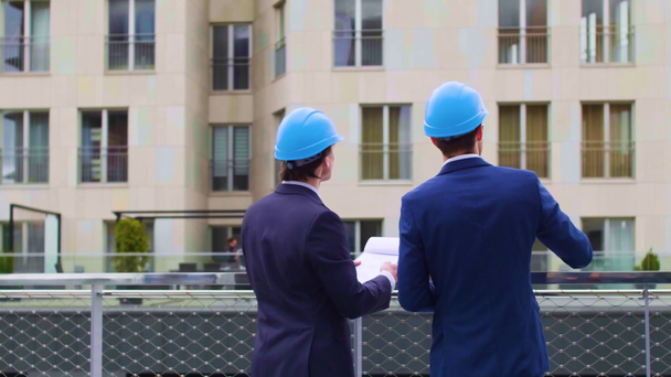 Real estate developers in helmets. New office construction. Confident business men and architect talking in front of modern office building. Businessman and his colleague have conversation. - Footage, Video