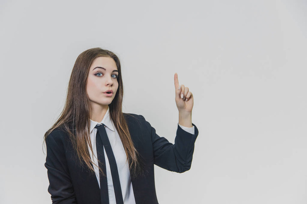 Young pretty businesswoman is pointing her finger up with an amusement, amazement and dazzling facial expression. - Foto, imagen