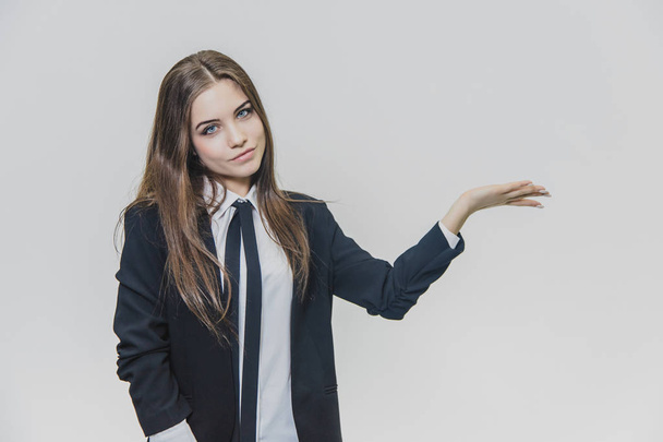 Serious thoughtful and thin smiled, brown-haired businesswoman is thinking while presenting something on the white background. - Фото, зображення