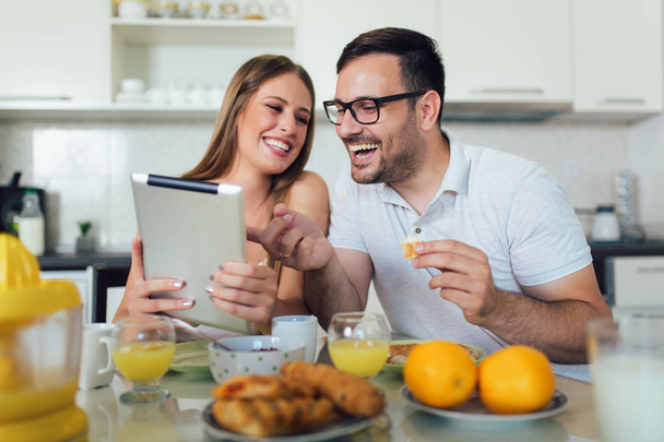 Felice coppia godendo il tempo della colazione insieme a casa e utilizzando
  - Foto, immagini