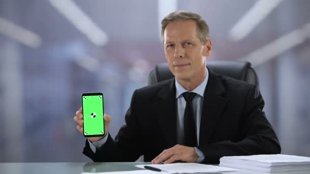 Joyful male boss in suit showing green screen smartphone at camera, business app - Metraje, vídeo