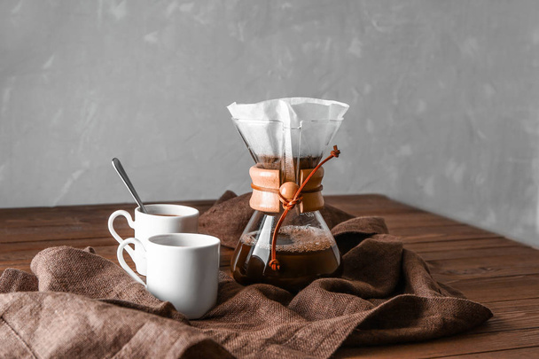 Вкусный кофе в химической и чашки на деревянном столе
 - Фото, изображение