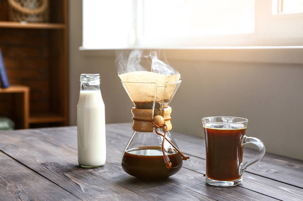 Вкусный кофе в химической и чашки с бутылкой молока на деревянном столе
 - Фото, изображение