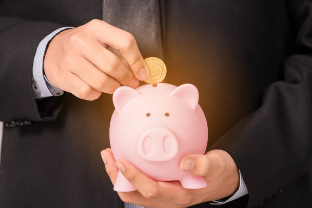 Close up of businessman insert gold coin into  piggy bank - Foto, imagen