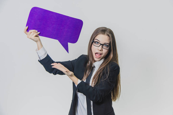 Young woman is holding a violet speech bubble over herself, which is rectangular-shaped, isolated, on the white background. Young lady is looking at the camera and presenting violet speech bubble - Zdjęcie, obraz