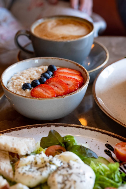 ヘルシーな朝食:ベリーのオートミール、チェリートマトとポーチドエッグのサラダ、カプチーノ1杯 - 写真・画像