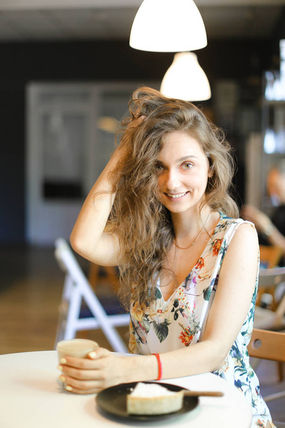 Jonge blanke vrouw zittend met cake en kopje koffie in café. - Foto, afbeelding