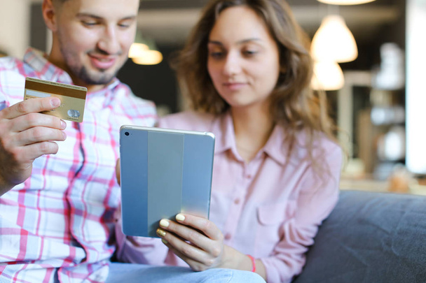 Mujer joven y hombre usando tableta y tarjeta de débito en la cafetería
. - Foto, imagen