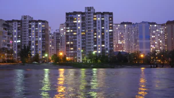 Complejo de edificios de apartamentos en la ciudad nocturna cerca del gran lago, con farolas reflejándose en el agua. Edificios en el crepúsculo cerca del lago. Edificios y luces en apartamentos por la noche
. - Metraje, vídeo